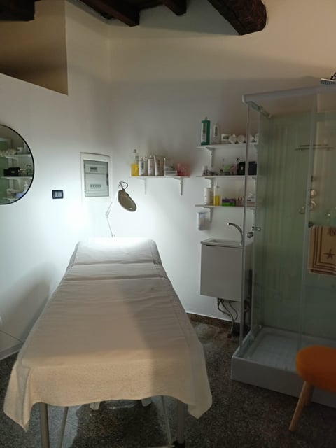 Minimalist spa or massage room with a treatment bed, wall shelves, sink, and shower enclosure with green glass door