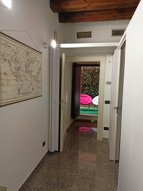 Narrow hallway with white walls and exposed wooden beam ceiling leading to outdoor patio with pink umbrella and green furniture