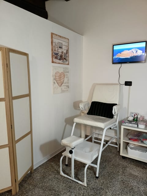 Modern medical or pedicure room with white furniture, wall art, and TV display showing a mountain landscape