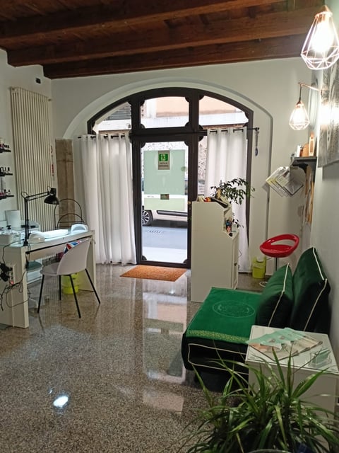 Interior of a modern office or studio space with polished concrete floors, black-framed glass doors, white curtains, exposed wooden beams, pendant lights, and green storage bins.